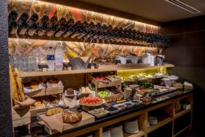 Een buffet met diverse soorten eten, waaronder fruit, groenten en brood. Ook staan er flessen en glazen op de planken.