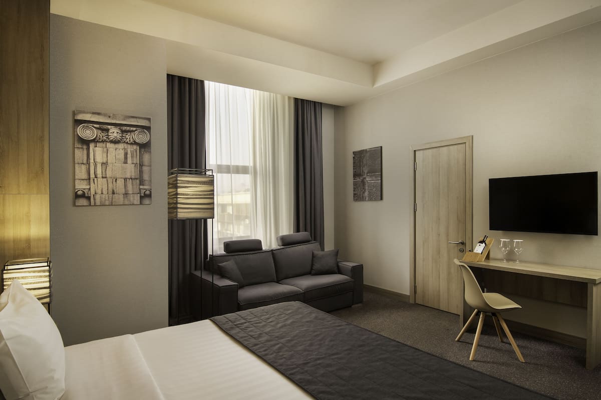 A modern hotel room with a bed, a sofa, a desk, and a TV.