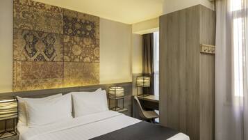 A hotel room with a bed, a desk, a chair, and a wall with patterned tiles.