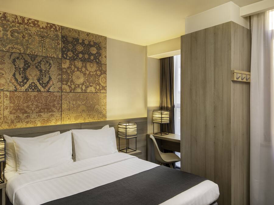 A hotel room with a bed, a desk, a chair, and a wall with patterned tiles.