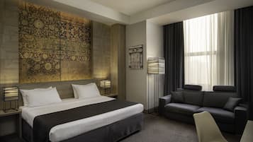 Una habitación de hotel moderna con una cama grande, un sofá, una silla y un adorno en la pared.