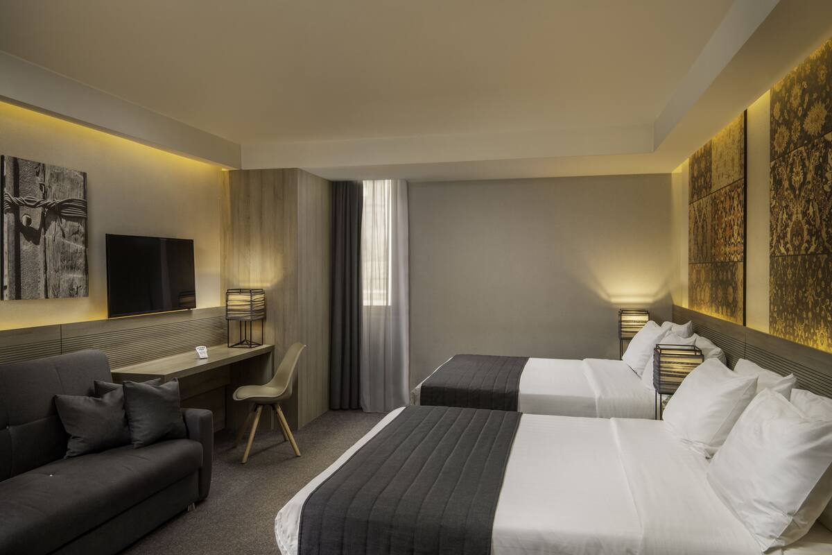 A hotel room with a bed, a desk, a chair, and artwork on the walls.