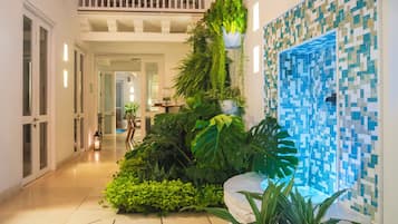 Um corredor com escada, um jardim vertical com diversas plantas e parede revestida por azulejos com padrão em mosaico azul.