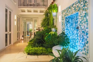 A hallway with a staircase, a wall-mounted planter with various plants, and a tiled wall with a blue mosaic pattern.