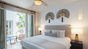 Quarto de hotel com cama, duas luminárias laterais, ventilador de teto e vista para uma varanda com plantas.