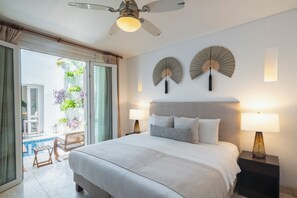 A hotel room with a bed, two bedside lamps, a ceiling fan, and a view of a balcony with plants.