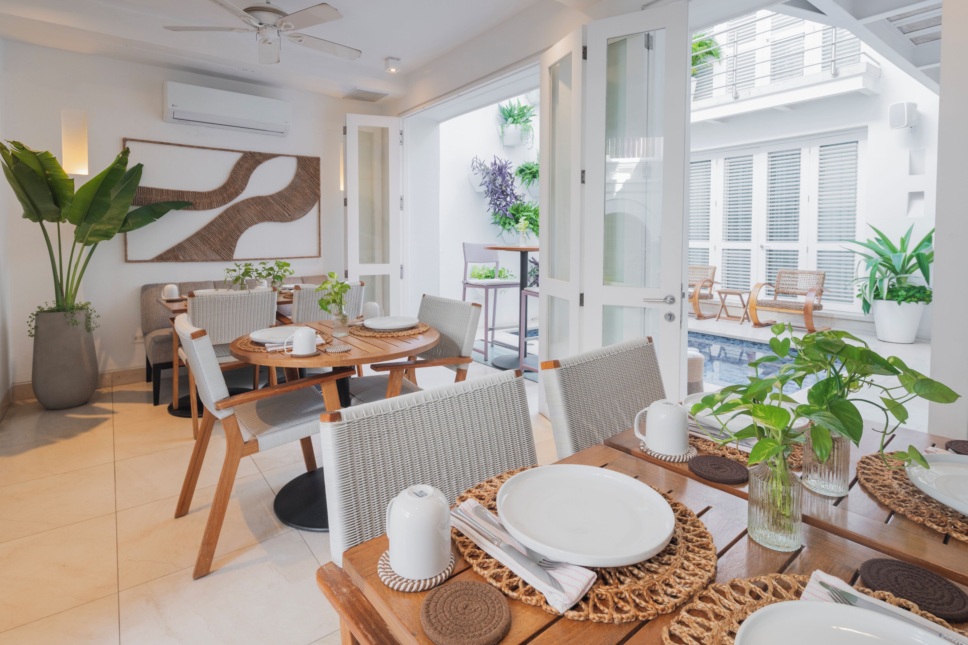Uma sala de jantar com mesa redonda posta para quatro pessoas, rodeada por cadeiras de vime.