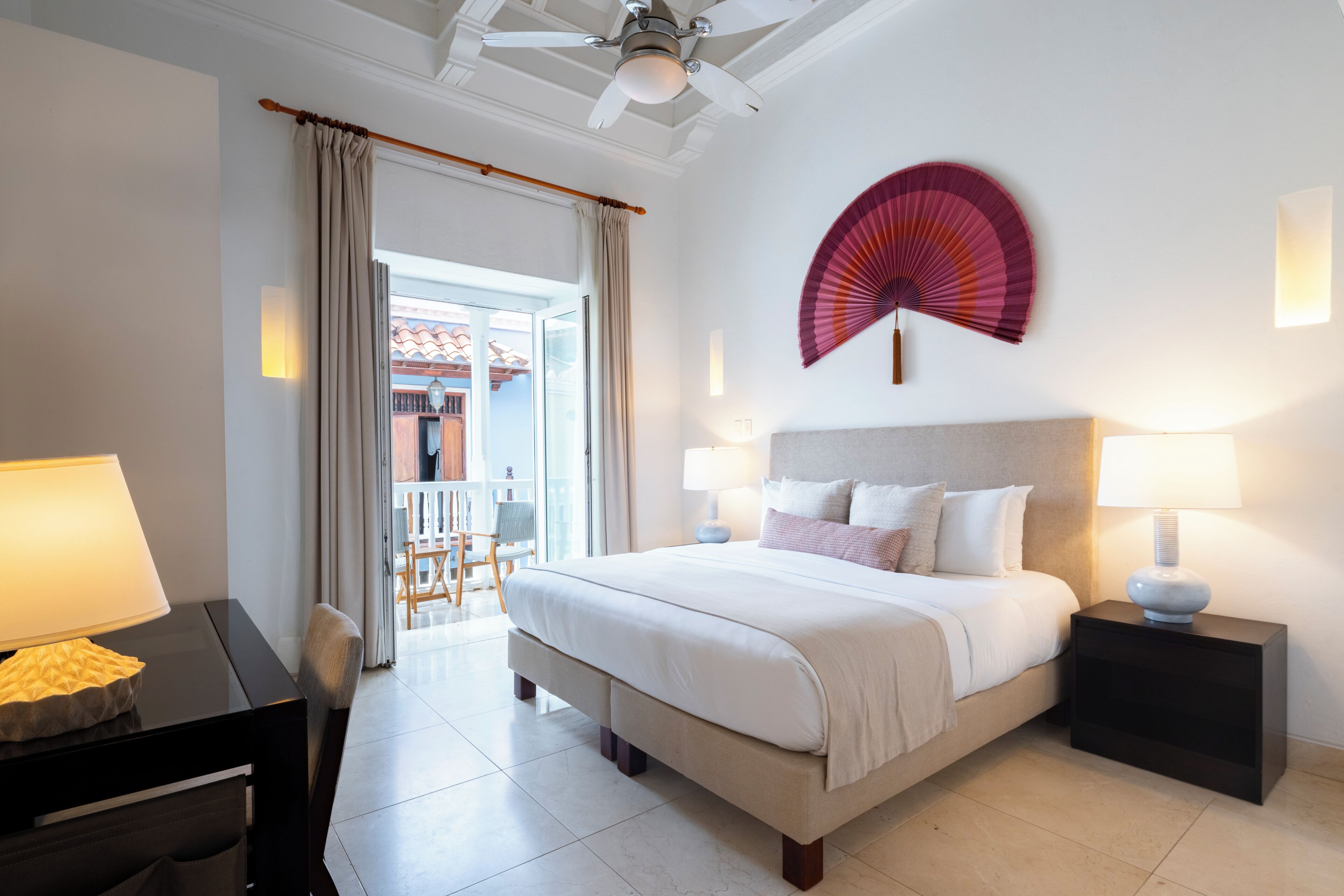 Una habitación de hotel con una cama, lámparas de noche, un ventilador y vistas al exterior.