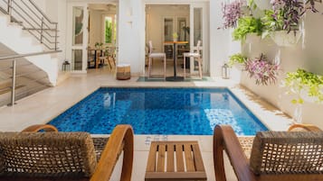 Un área de piscina con una piscina azul cristalina, sillones de madera para tomar el sol y una mesa.