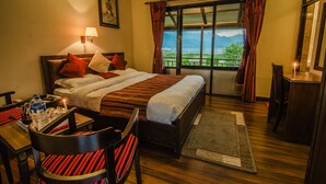 A hotel room with a bed, a desk with a chair, a nightstand, a lamp, and a window with curtains. - Hotel Lakefront (Pokhara)
