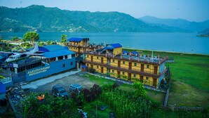 A hotel with a blue and yellow exterior, located near a body of water with mountains in the background. - Hotel Lakefront (Pokhara)