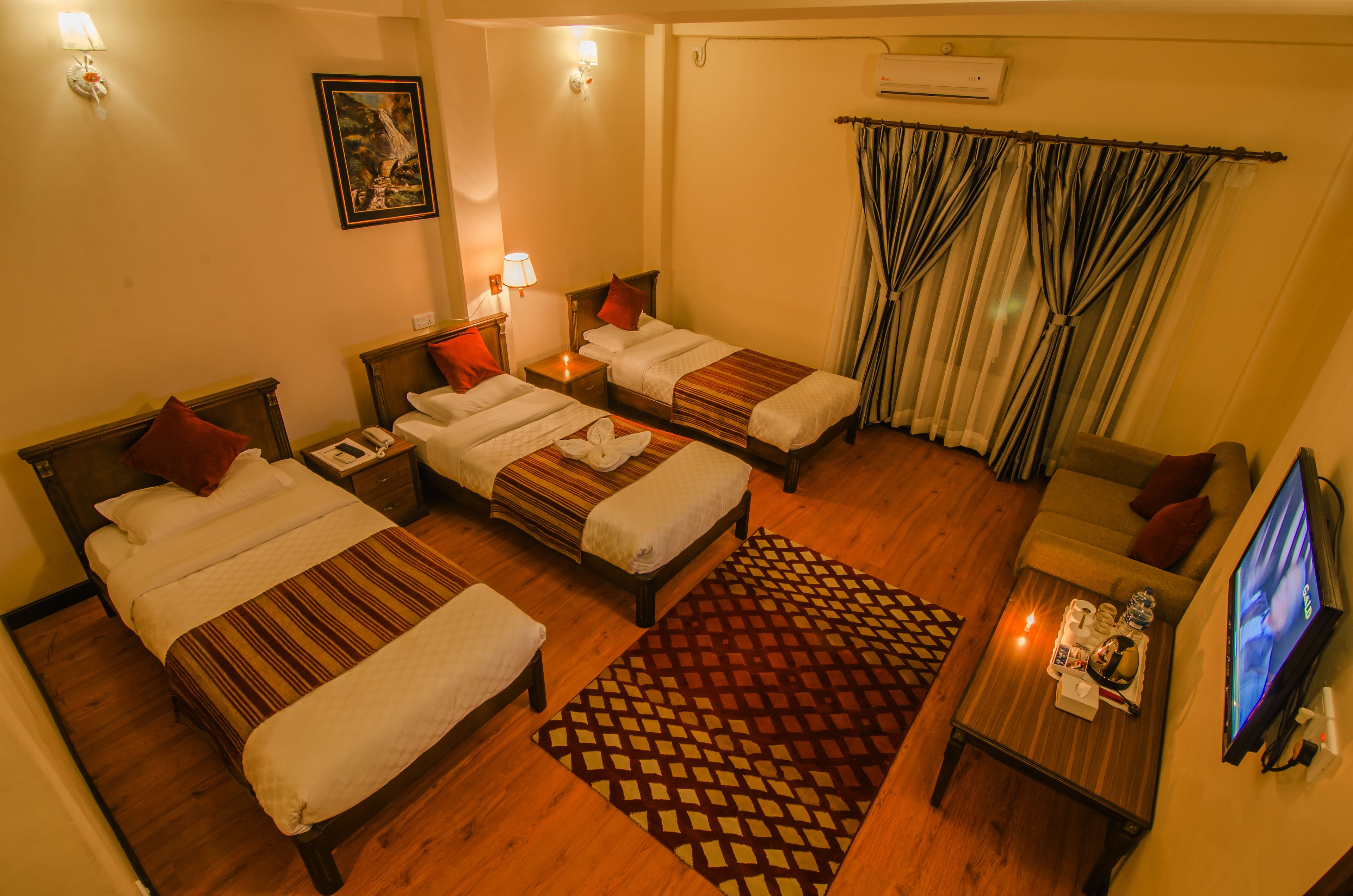 A hotel room with two beds, a sofa, a TV, a coffee table, and a patterned rug.