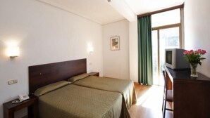 Habitación de hotel con dos camas, un escritorio con televisor, teléfono y ventana con cortinas.