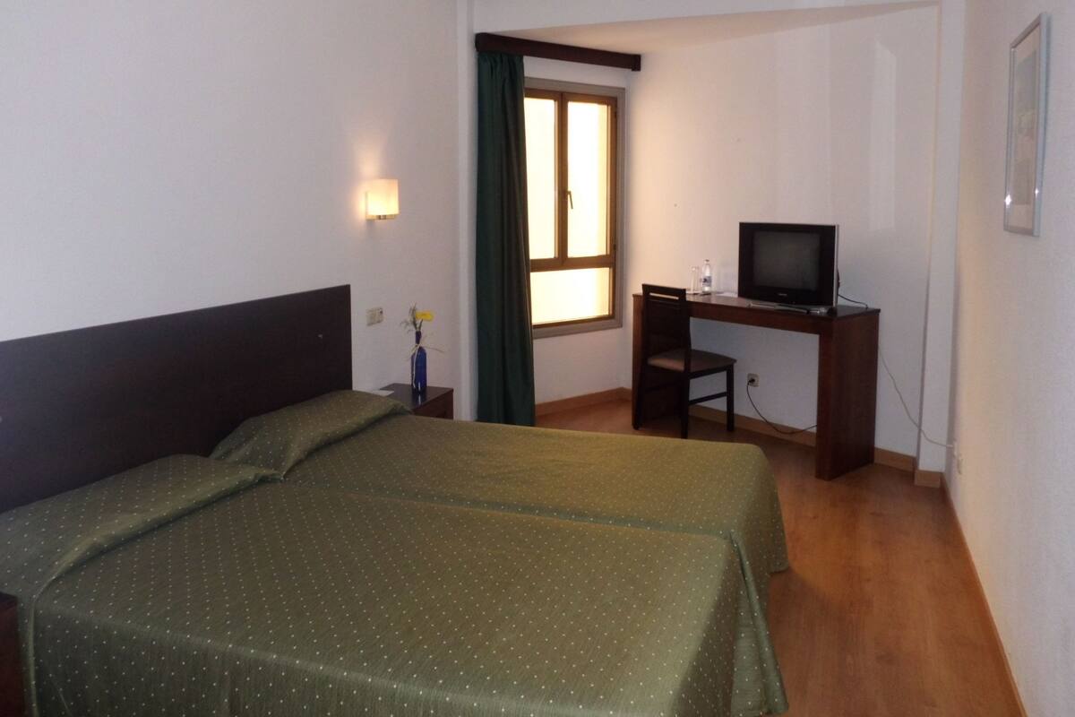 A hotel room with a bed, a desk with a television, and a window with curtains.