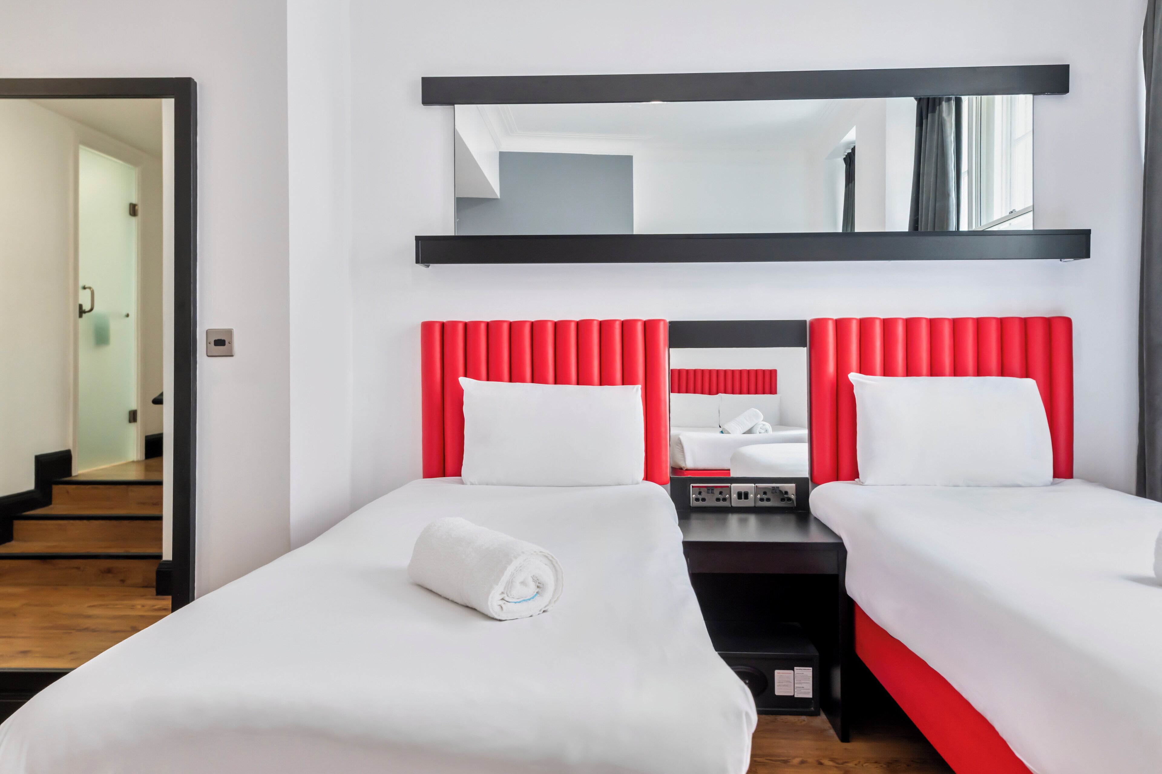 A hotel room with two beds, a large mirror, and a wooden staircase.