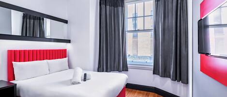 A modern hotel room with a red bed, white bedding, a large window with black curtains, a black nightstand, and a red accent wall.