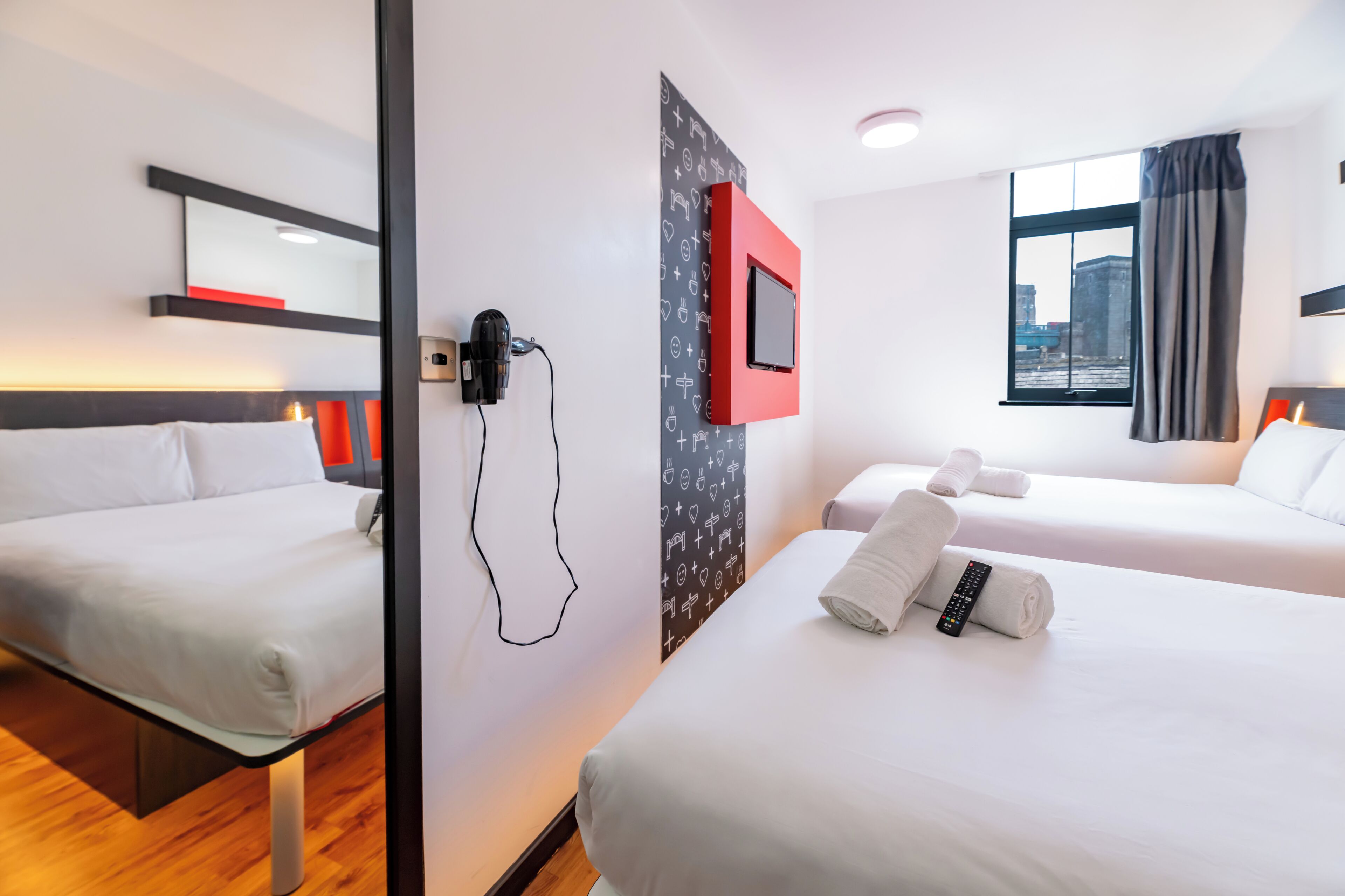 A hotel room with two beds, a TV mounted on the wall, and a window with curtains.