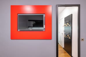 Habitación de hotel moderna con una pared de acento roja, una puerta con perchas de madera y un pasillo con piso de madera.