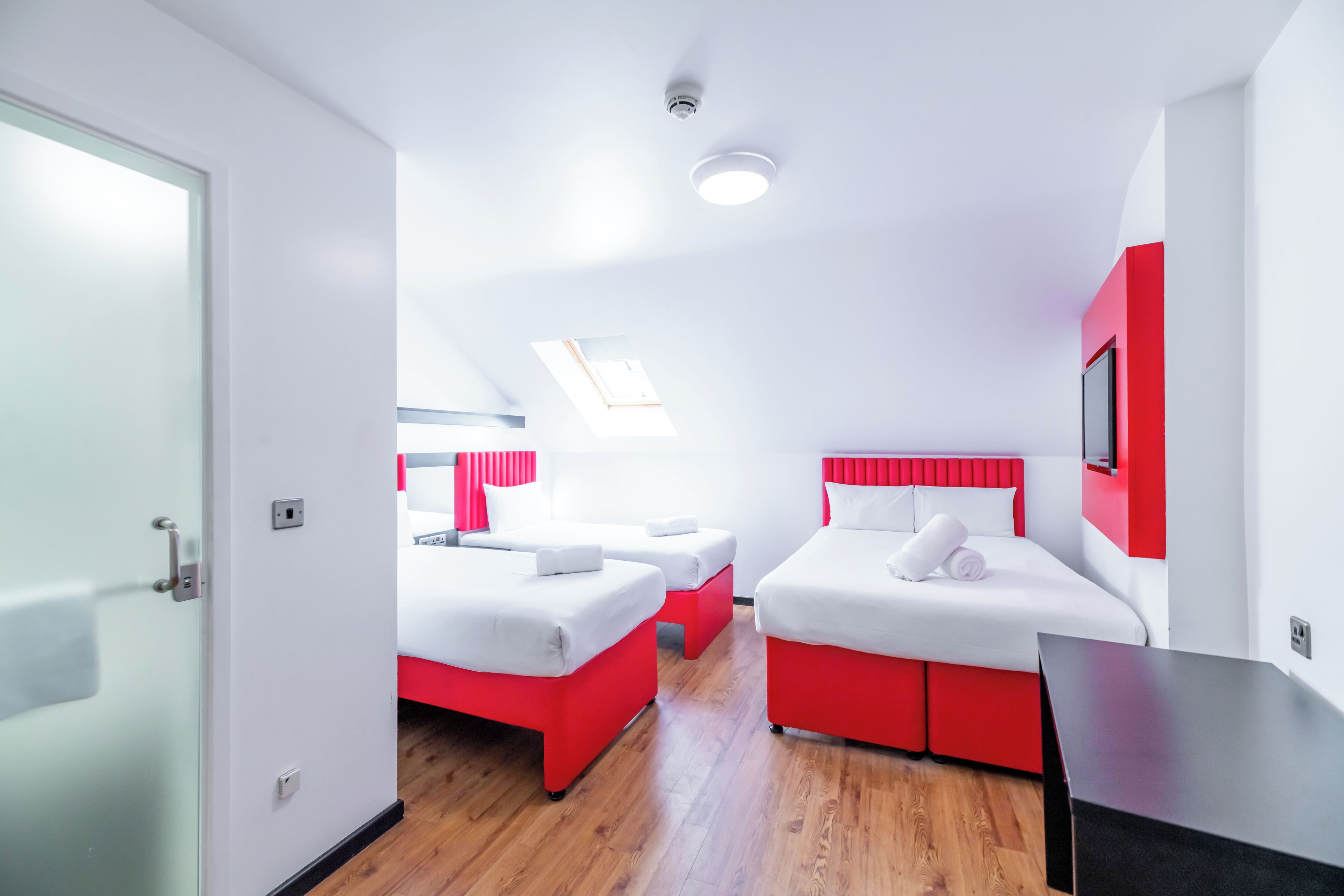 A modern hotel room with two beds, a TV, and a skylight.