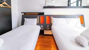 Quarto de hotel com duas camas, piso de madeira, cabeceira preta e espelho sobre as camas.