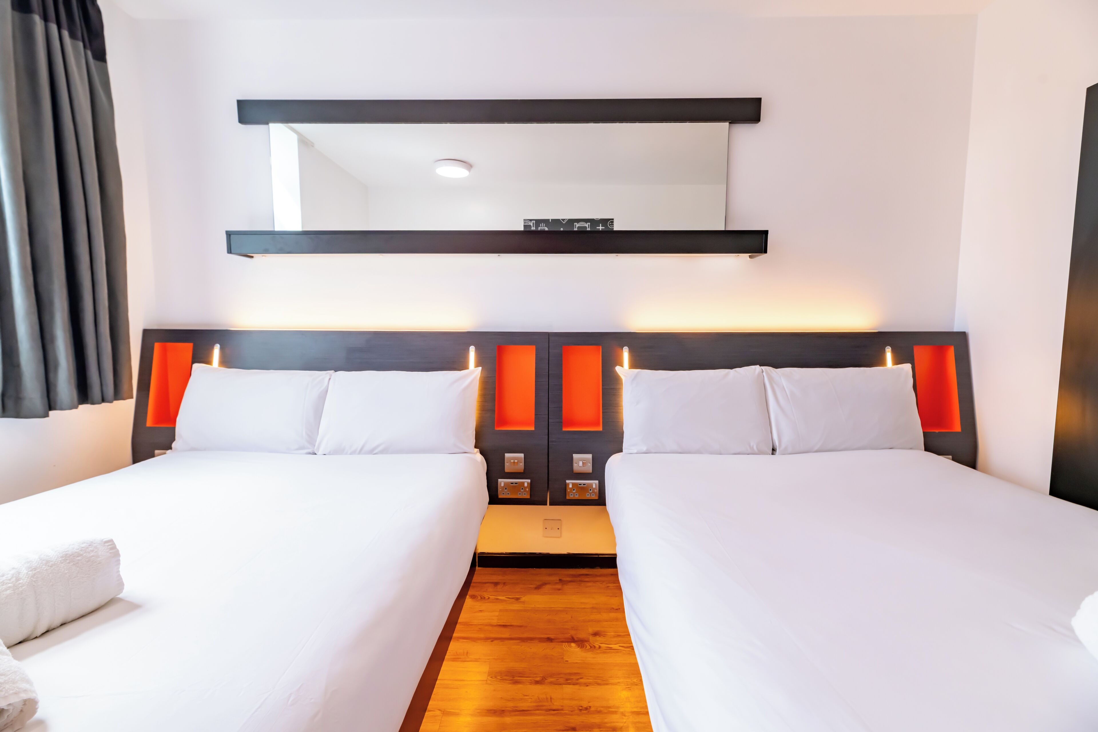 Een hotelkamer met twee bedden, een houten vloer, een grote spiegel boven de bedden en een modern bedkap.