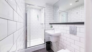 Un bagno moderno con piastrelle bianche, cabina doccia in vetro, lavandino e cestino.