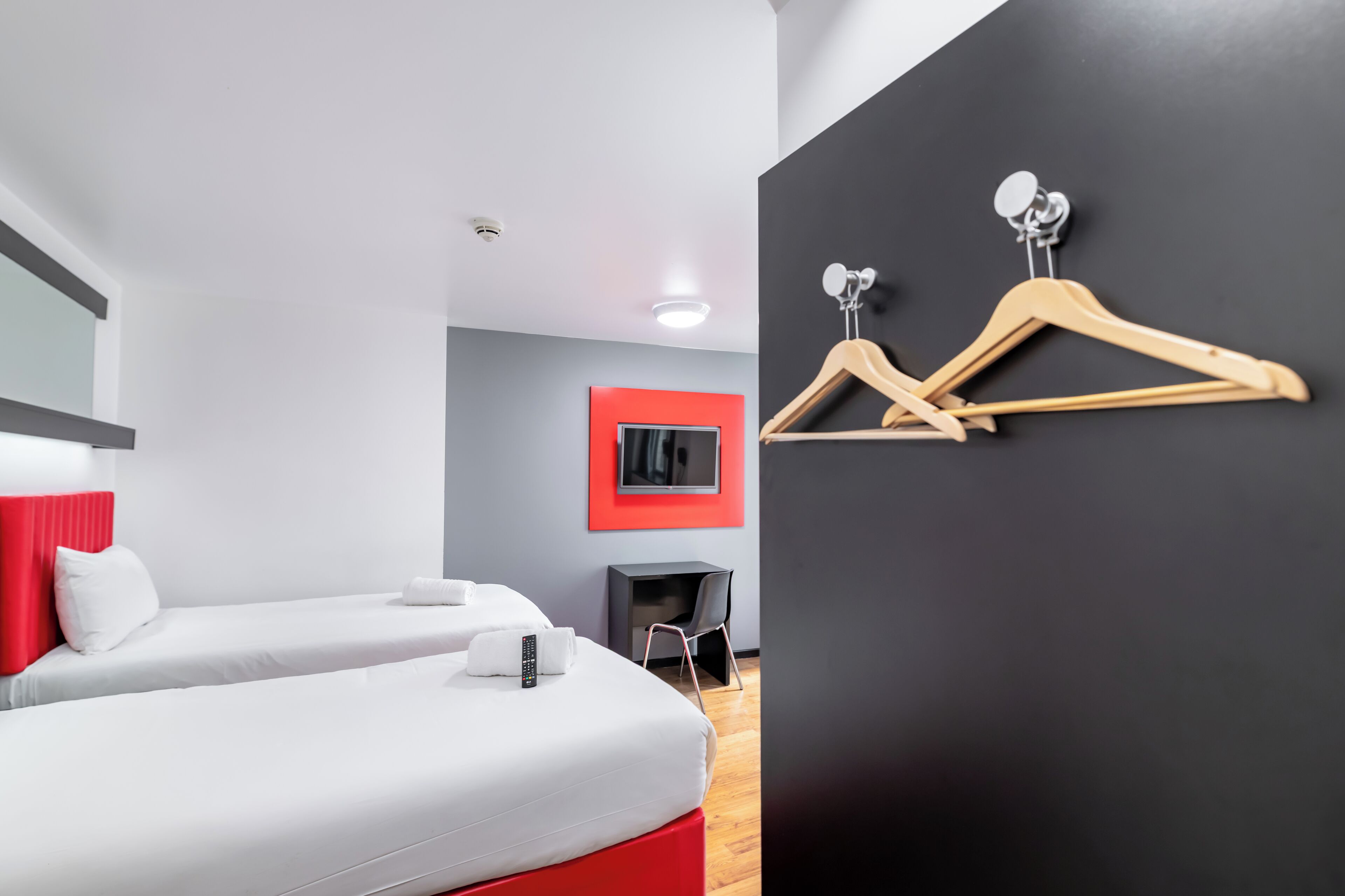 A modern hotel room with two beds, a TV, and a coat rack.