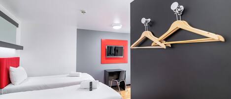 A modern hotel room with two beds, a TV, and a coat rack.
