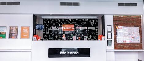 A reception desk with a 'Welcome' sign, a black wall with white icons, and a map on the right.