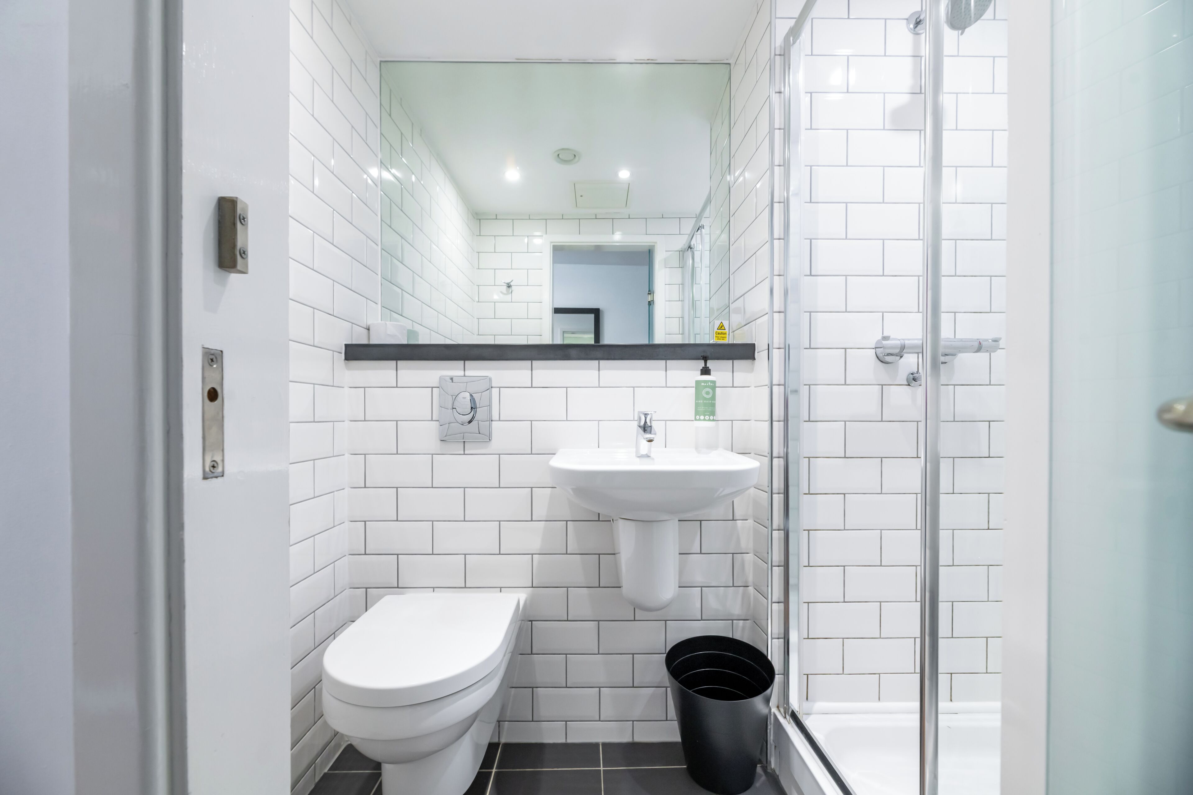 Un baño moderno con paredes de azulejos blancos, un inodoro blanco, un lavabo con espejo y una cabina de ducha de vidrio.