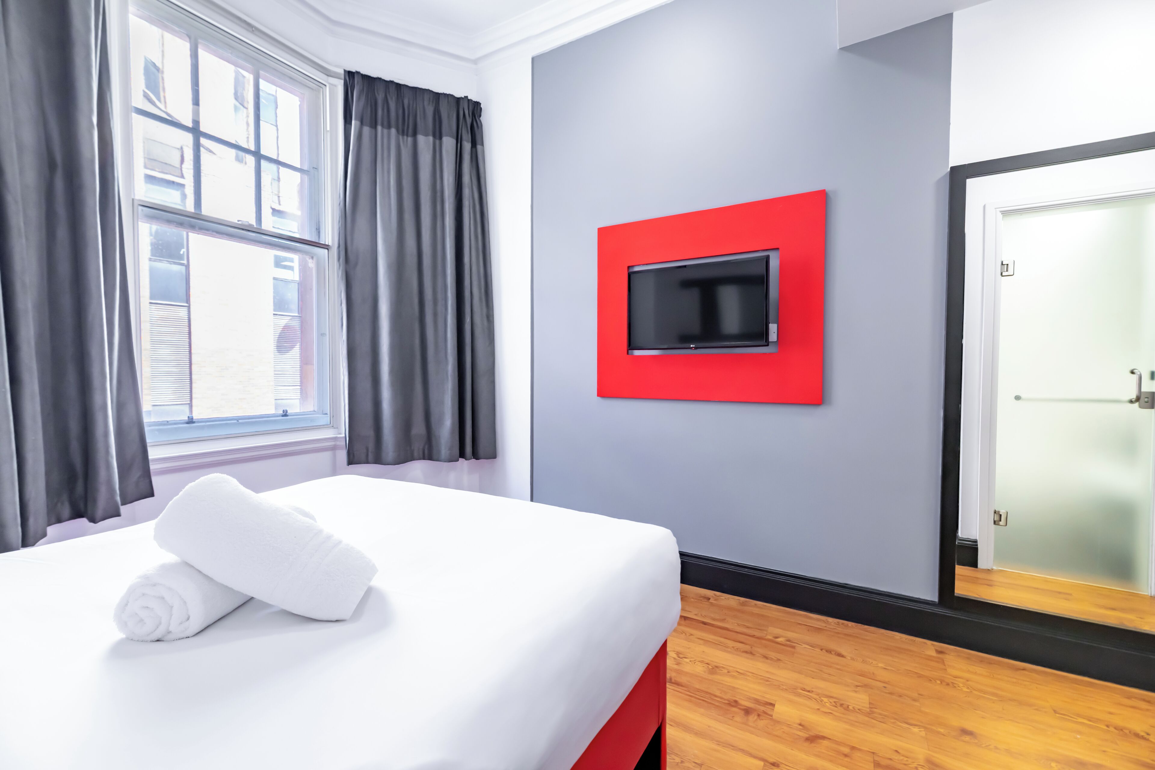 A hotel room with a bed, a TV mounted on a grey wall, and a door with frosted glass panels.