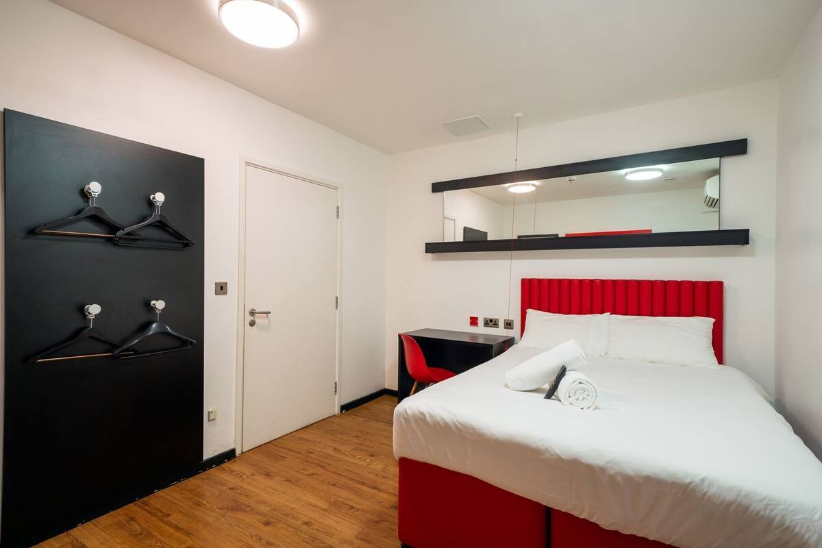 A hotel room with a bed, a desk, a chair, a wardrobe, and a mirror.
