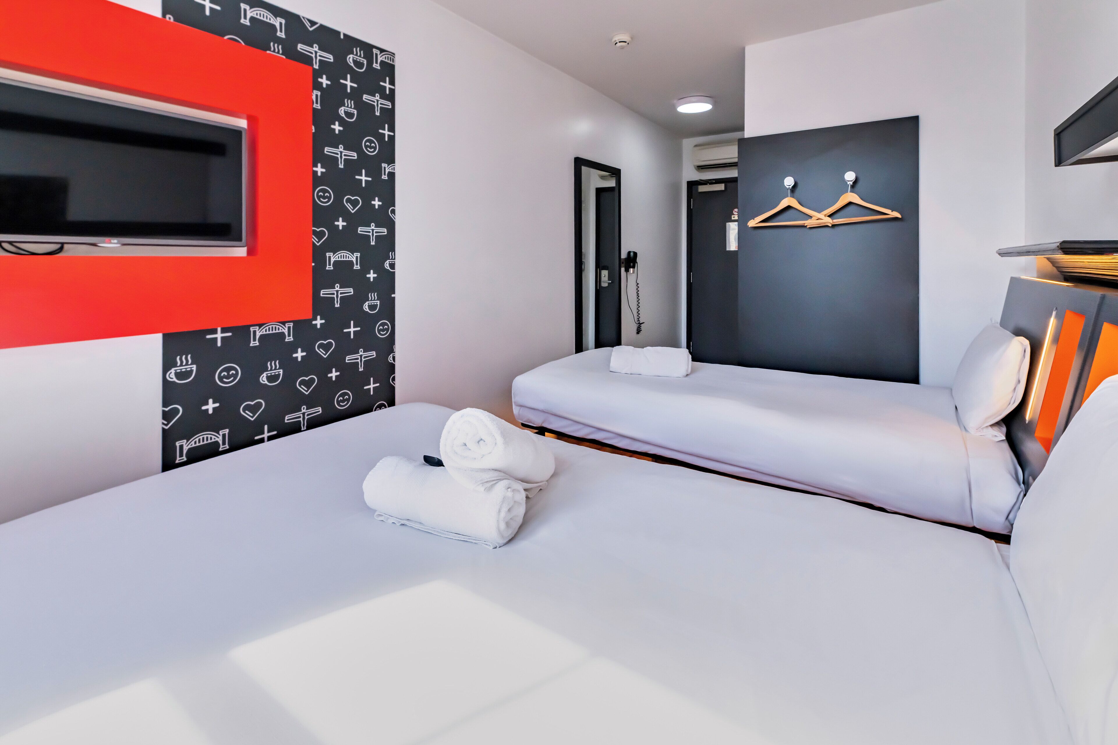 Habitación de hotel moderna con una cama grande, televisor montado en la pared, un espejo y un armario con ropa colgada.
