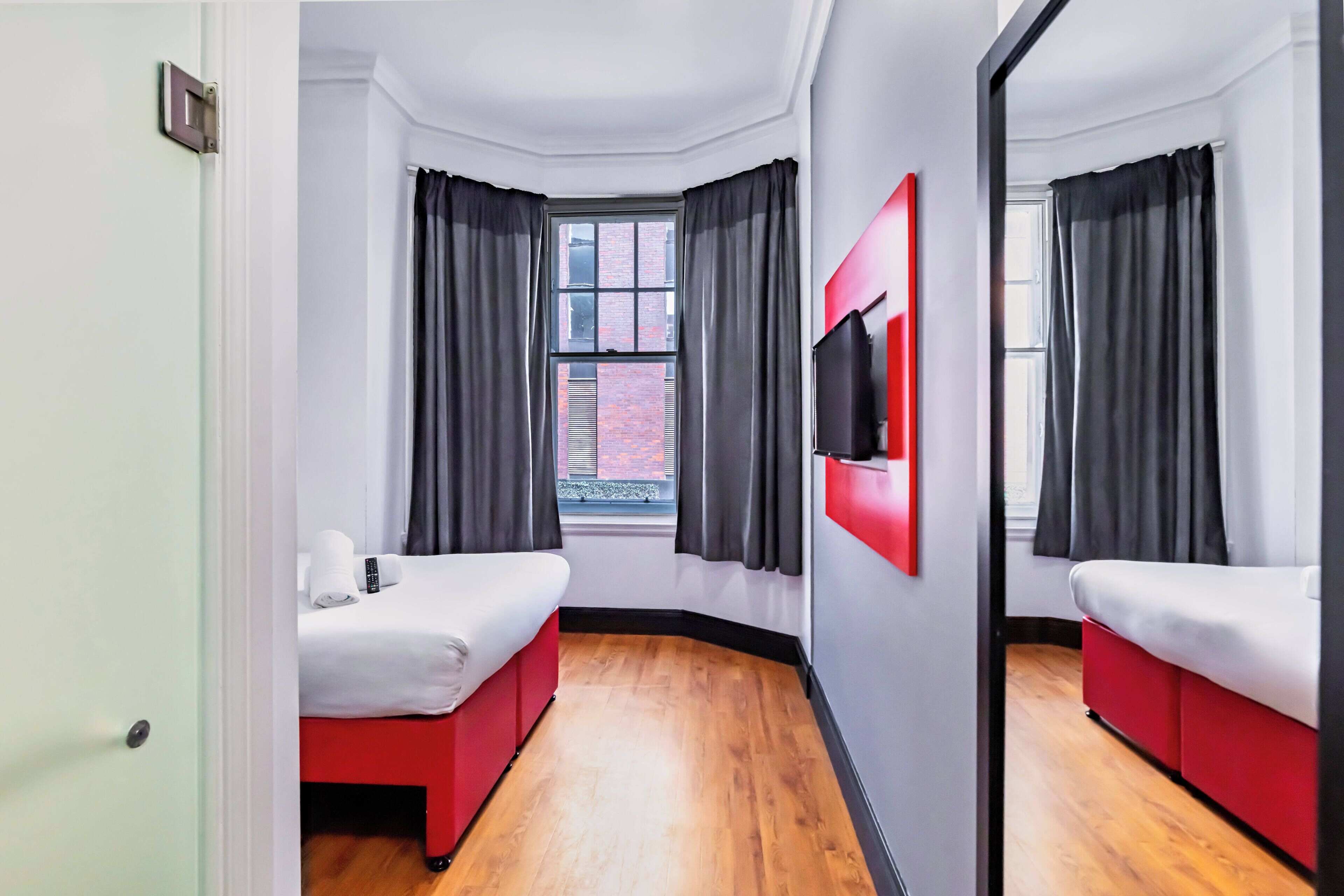 Habitación de hotel con dos camas, un espejo grande y una ventana con cortinas negras.