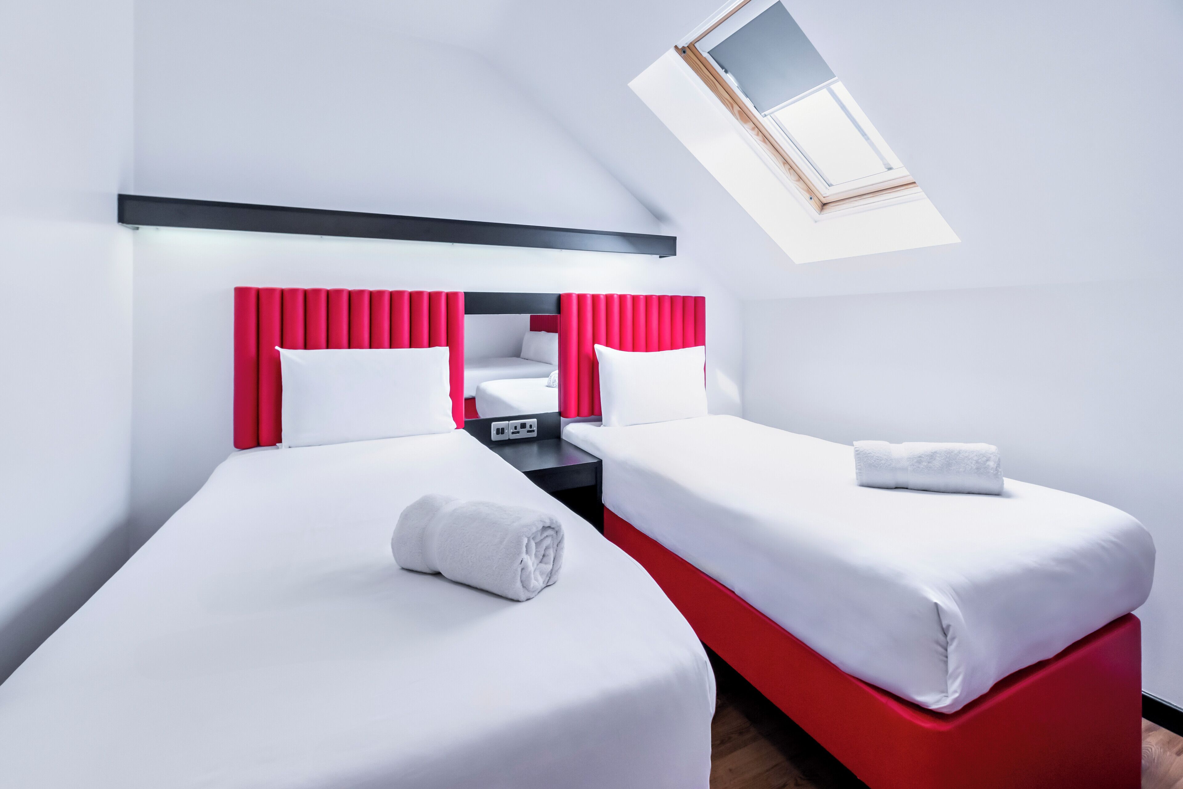 A hotel room with two beds, a skylight, and a red accent wall.