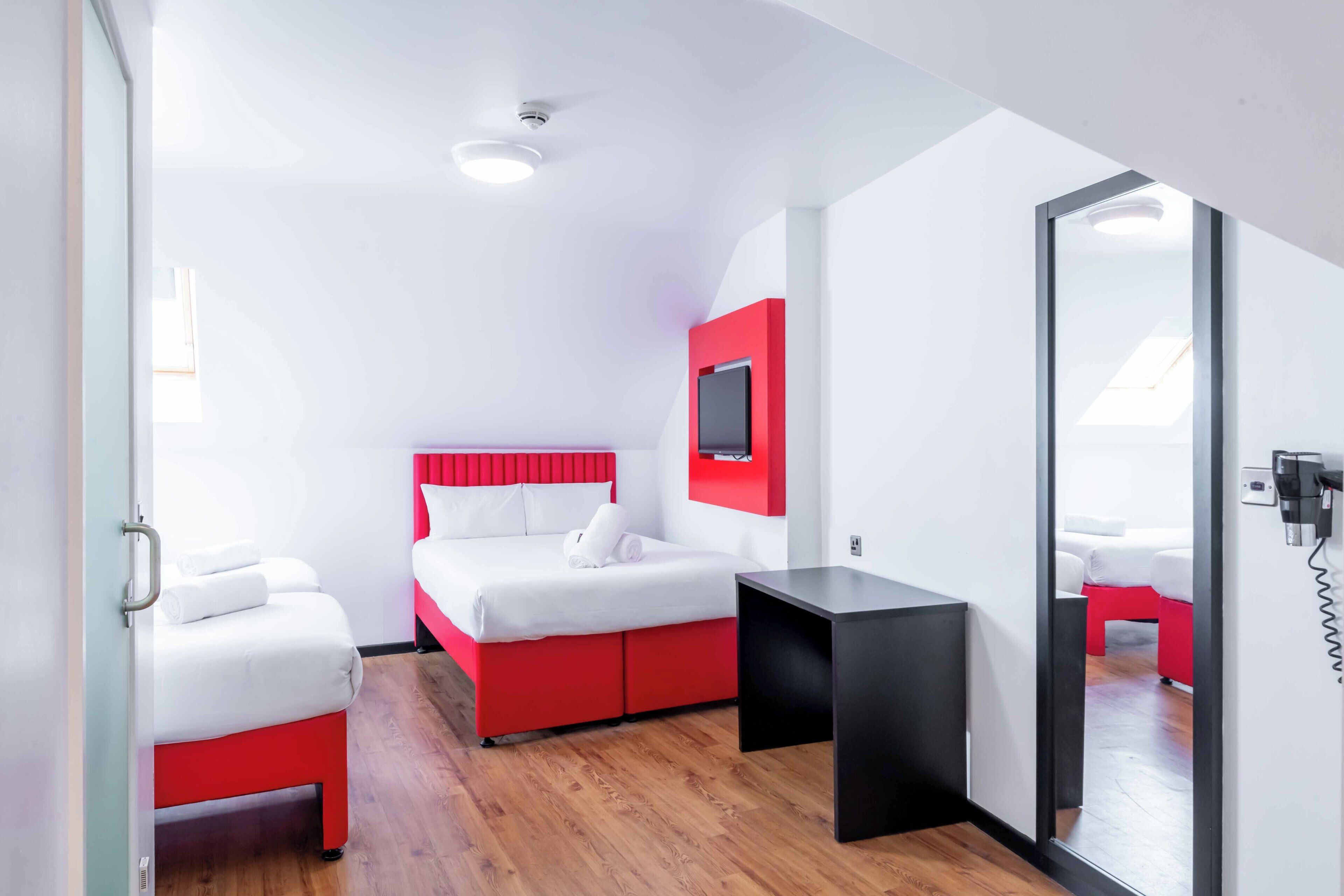 A hotel room with a bed, a small table, a TV mounted on the wall, and a mirror.