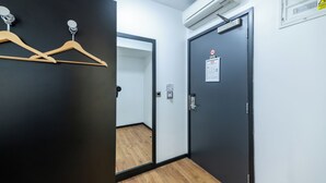 Quarto de hotel com piso de madeira, porta preta com sinal de segurança e unidade de ar condicionado na parede.
