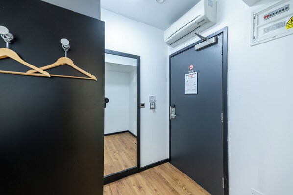 A hotel room with a wooden floor, a black door with a safety sign, and an air conditioning unit on the wall.