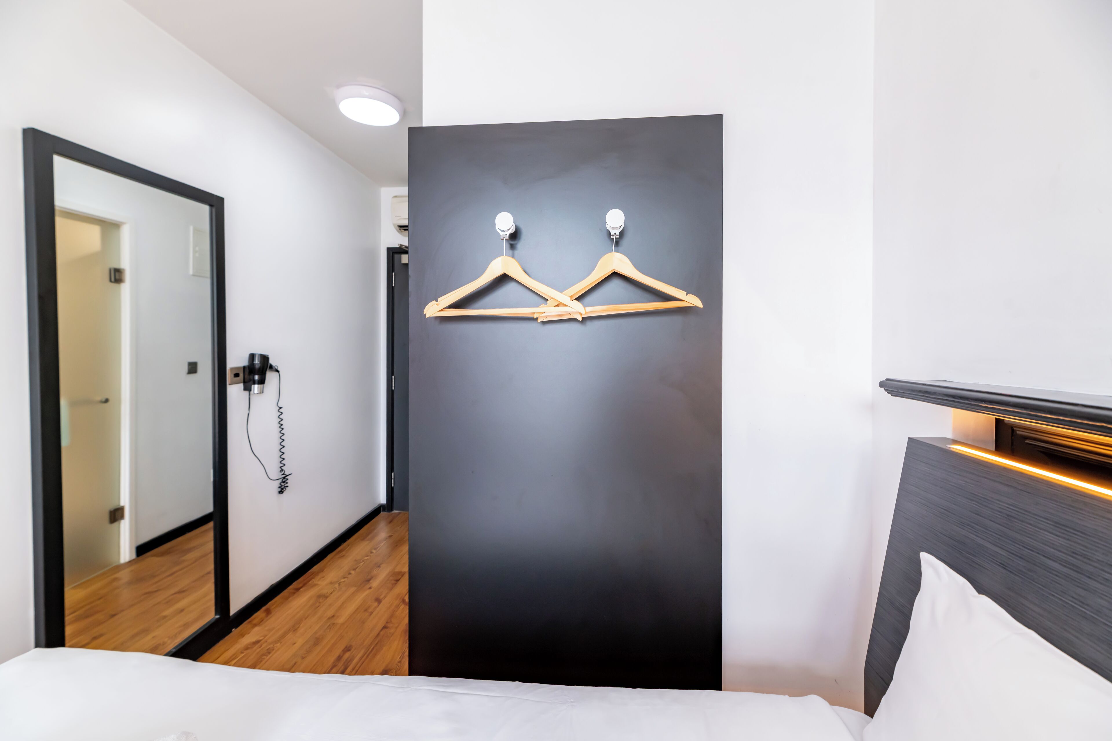 A hotel room with a bed, a dark wall with wooden hangers, a wooden floor, and a door with a phone.