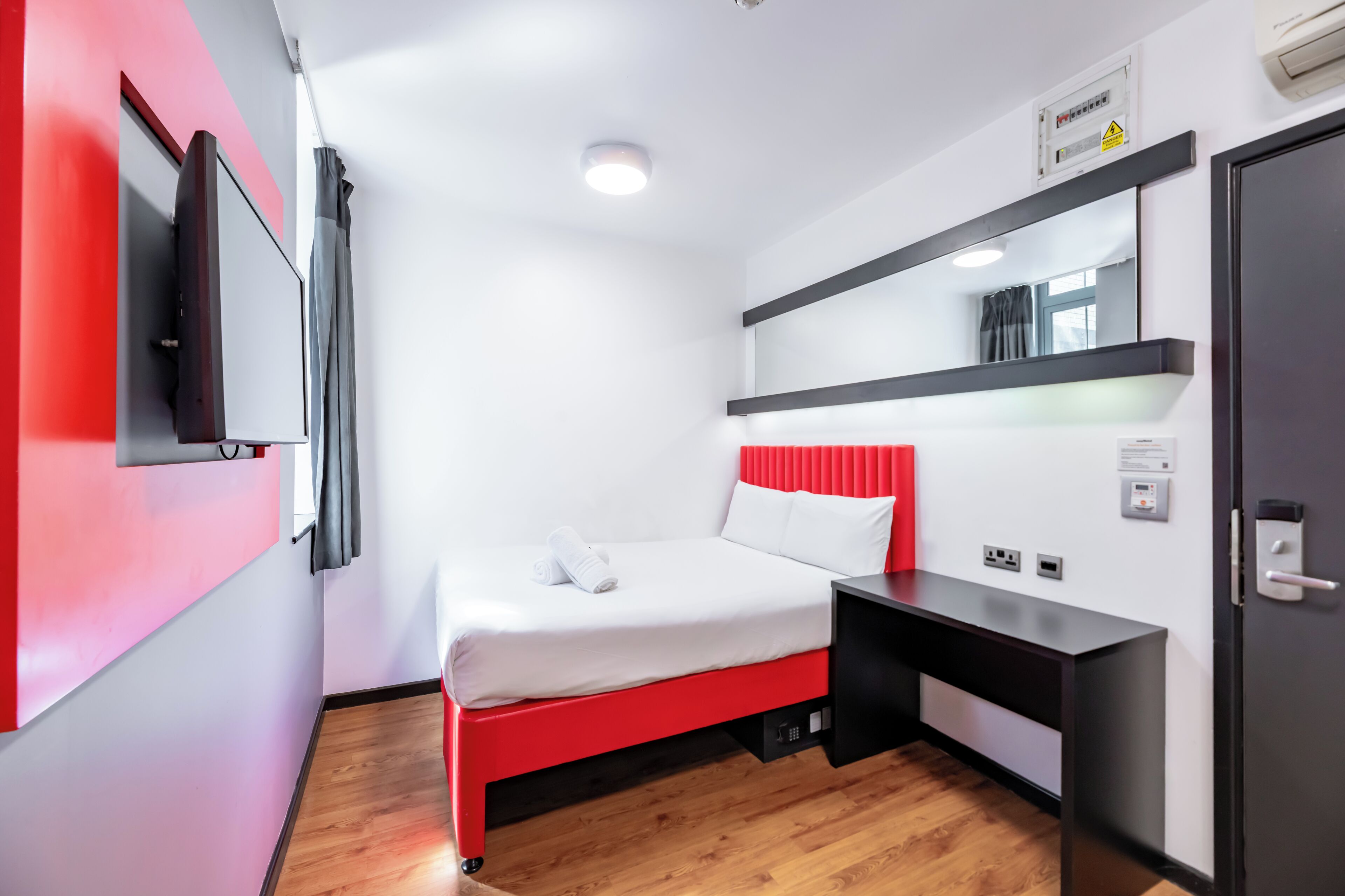 A modern hotel room with a bed, a desk, a flat-screen TV, and a mirror.
