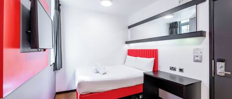 A modern hotel room with a bed, a desk, a flat-screen TV, and a mirror.