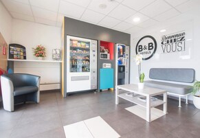 Un espace d’accueil d’hôtel comprenant un coin salon, des distributeurs automatiques et une enseigne B&B Hotels.