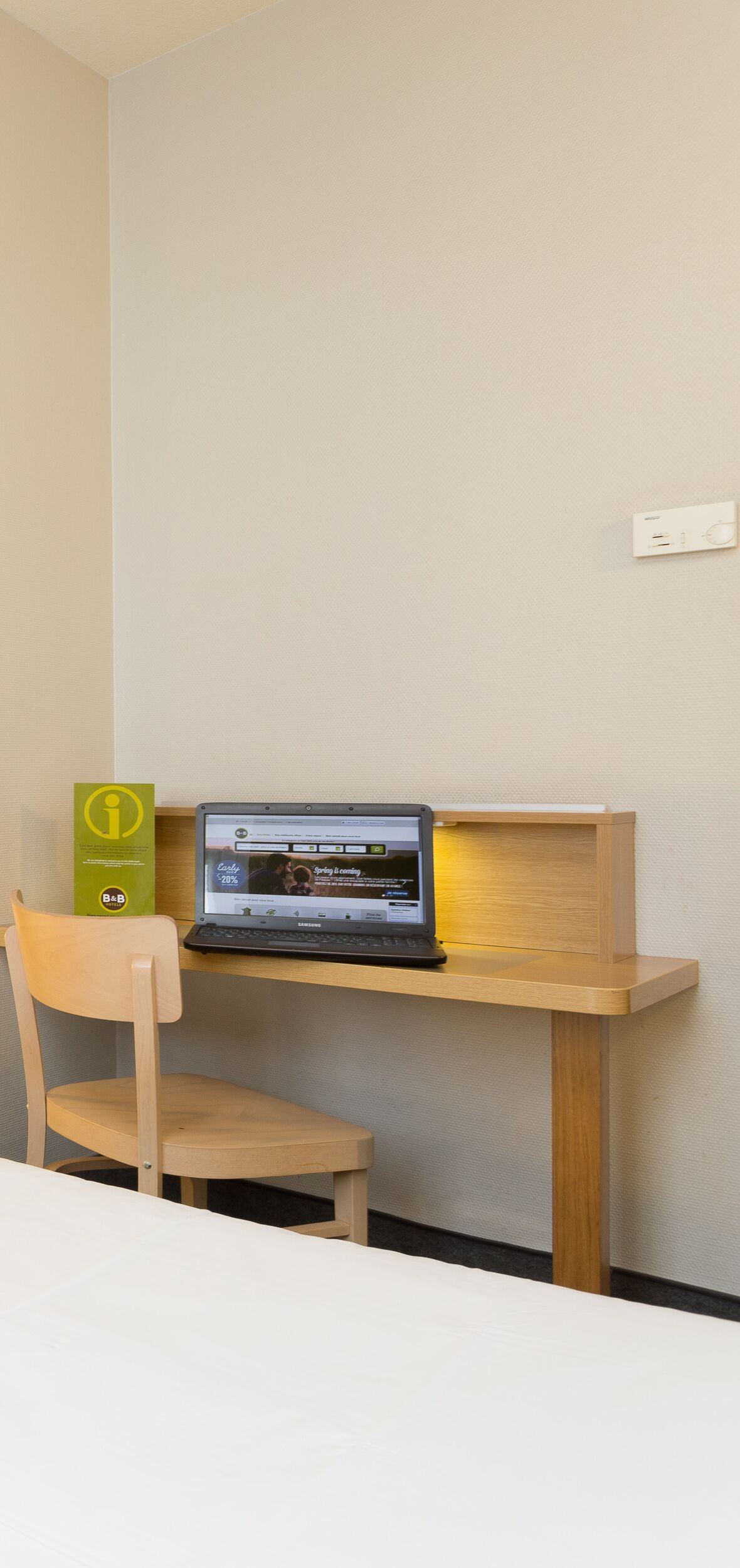 A workspace with a laptop on a wooden desk, a chair, and a small green information stand.