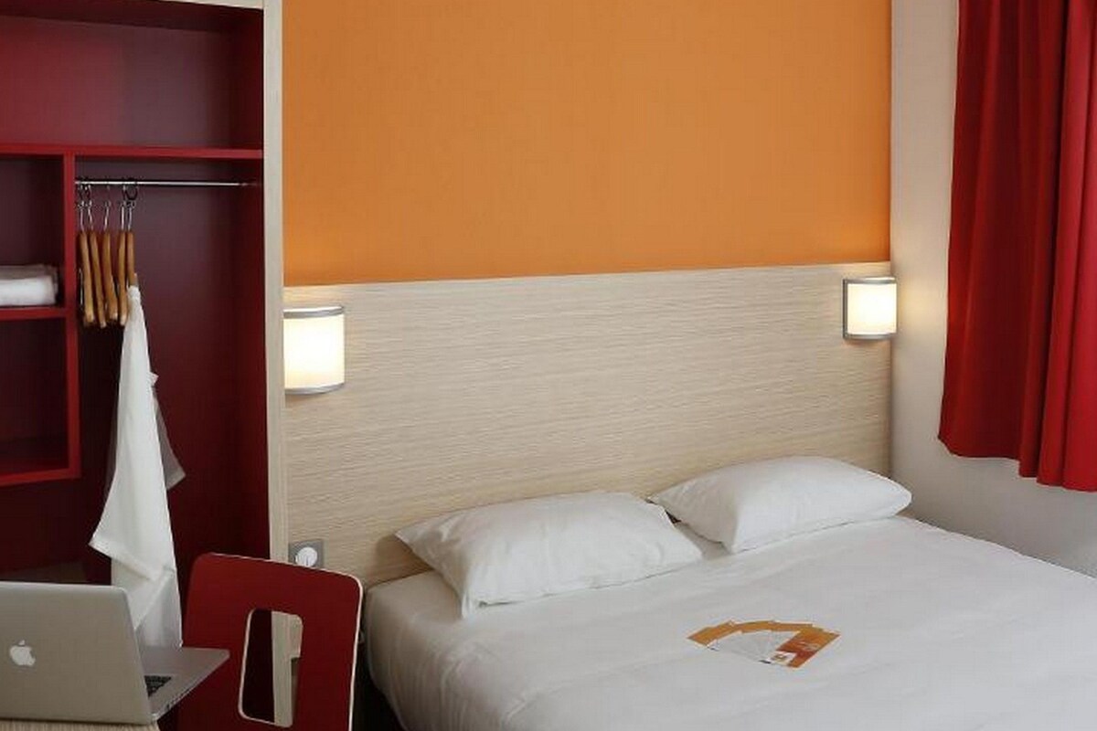 Une chambre d’hôtel comprenant un lit, un bureau avec un ordinateur portable, une chaise et une armoire.