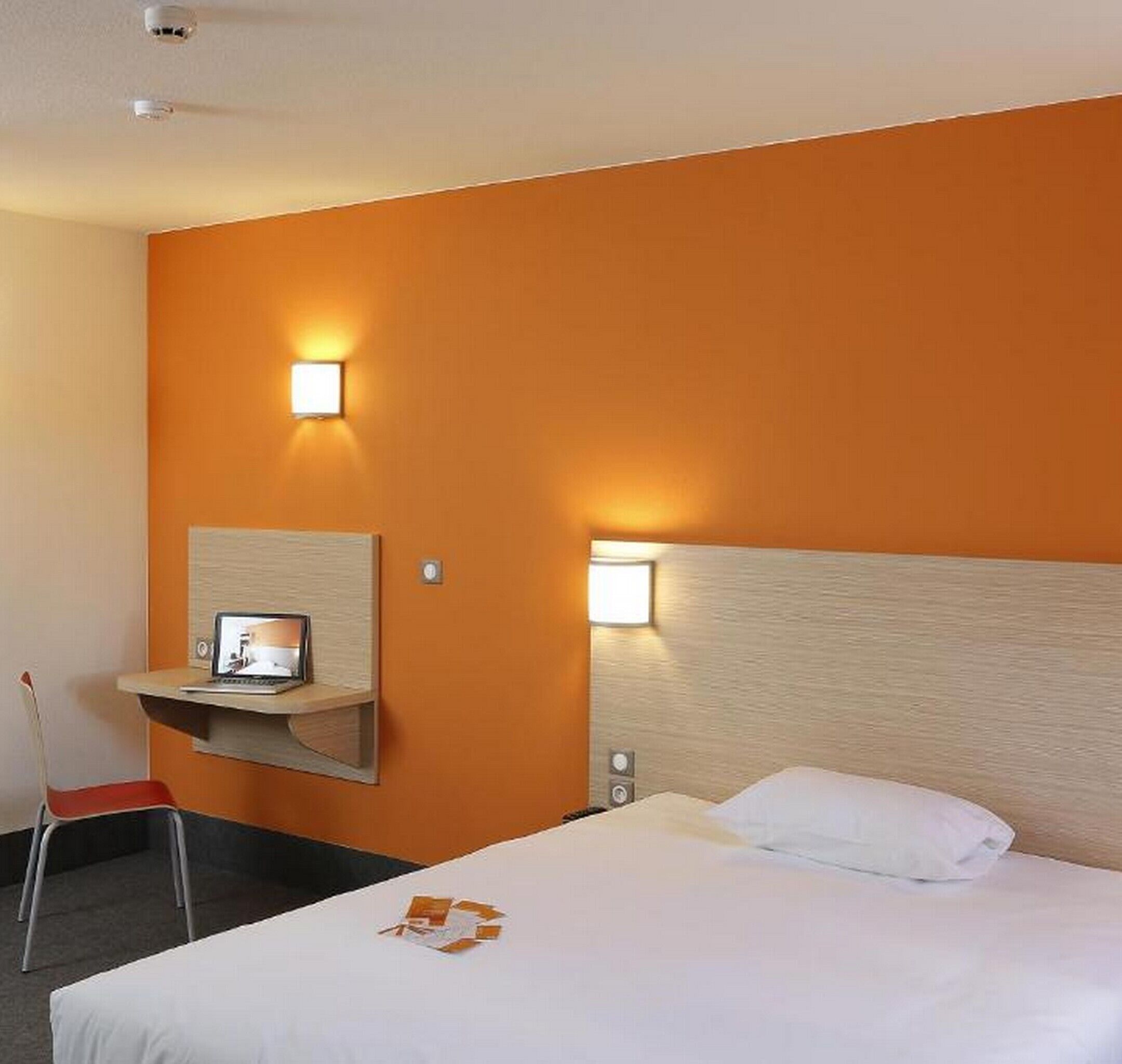 Een hotelkamer met een bed, een bureau met een laptop, twee wandlampen en een stoel.