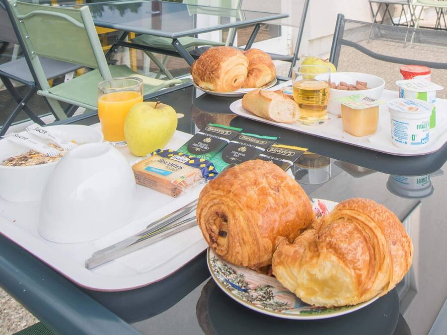 Een ontbijtkarretje met croissants, sinaasappelsap en ontbijtgranen op een tafel.