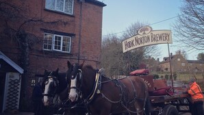 Un carruatge tirat per cavalls amb un cartell que diu "Hook Norton Brewery" davant d'un edifici de maó.