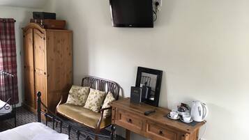 Ein Hotelzimmer mit einem Bett, einem Holztisch mit Wasserkocher, einem Stuhl, einem Kleiderschrank und einem flachen Fernseher an der Wand.