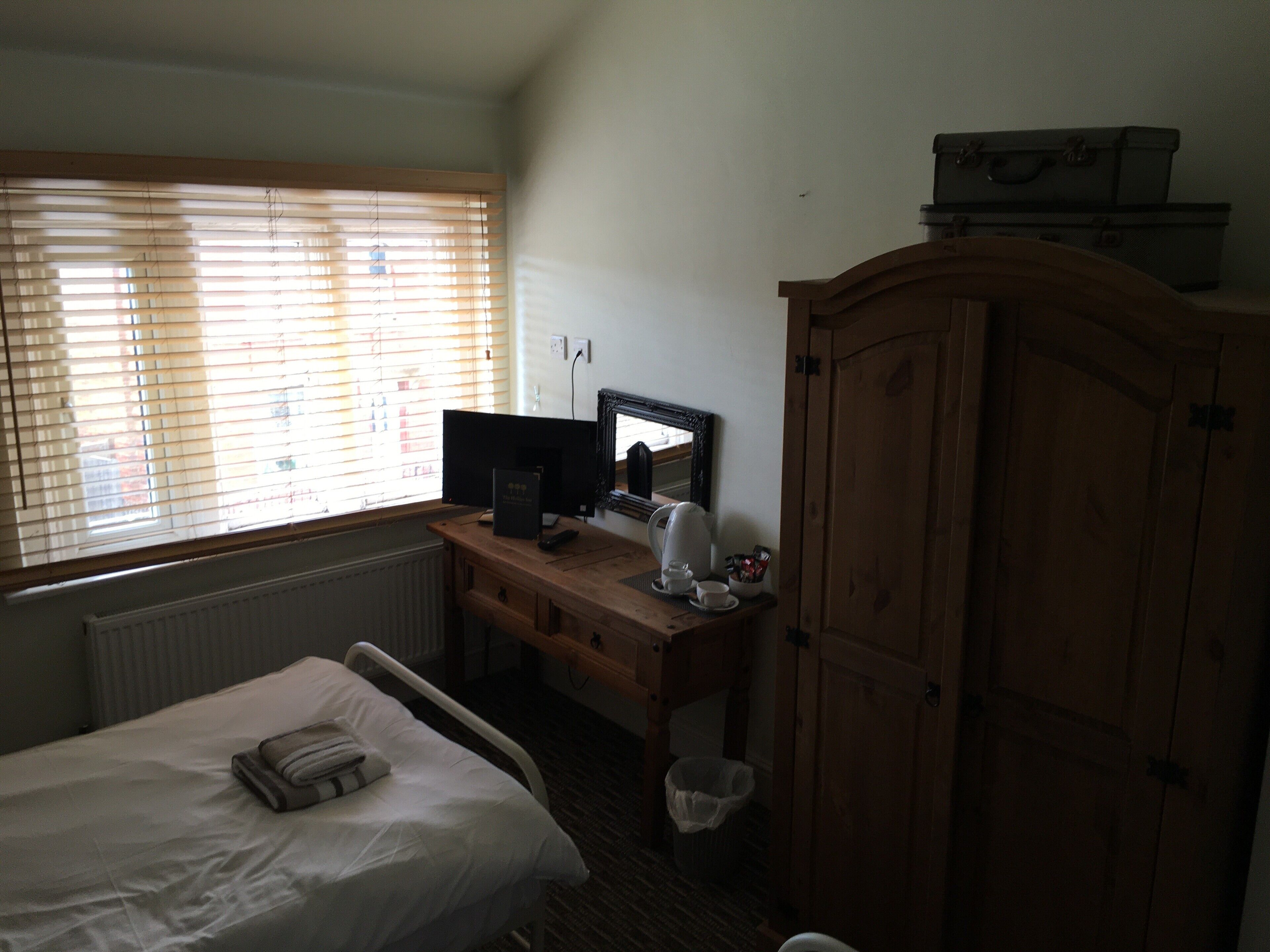 Een slaapkamer met een bed, een bureau met een computer, een spiegel en een kledingkast.