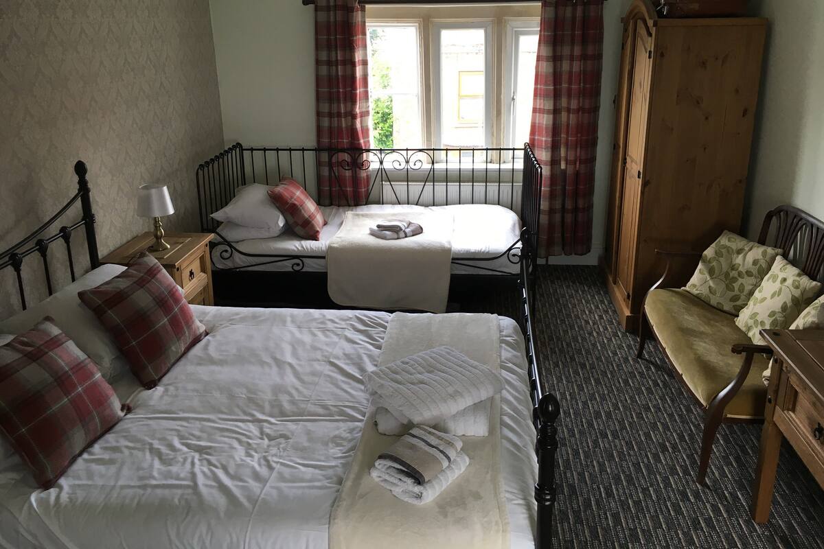 A room with two beds, a wooden wardrobe, a chair, and a window with curtains.